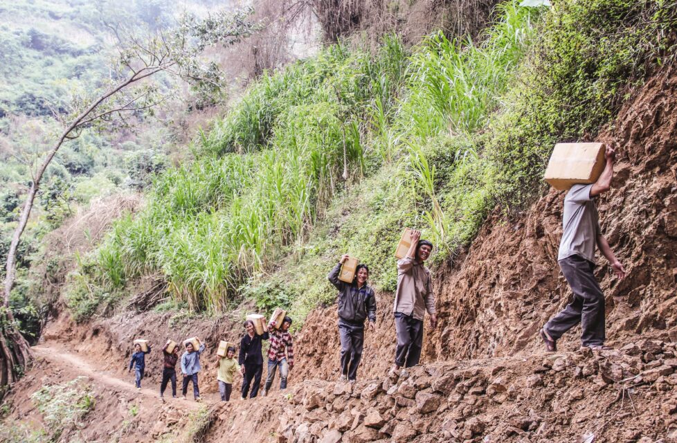 men smile as they carry boxes of supplies and bibles to their villages